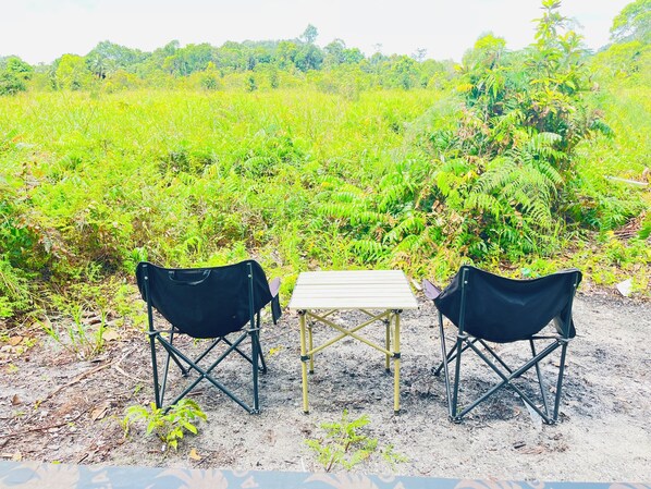 Two black folding chairs and a small table set up on a dirt path in a lush green field.