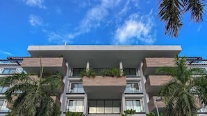 Un immeuble moderne à plusieurs étages, doté de balcons, d’une entrée pavée et entouré de verdure.