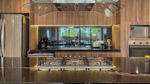 Une cuisine moderne dotée d’un îlot central, d’appareils électroménagers en acier inoxydable et d’une protection en verre pour la cuisinière.