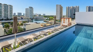Une piscine sur le toit, dotée de chaises longues, d’un auvent et offrant une vue sur le paysage urbain avec ses gratte-ciel.