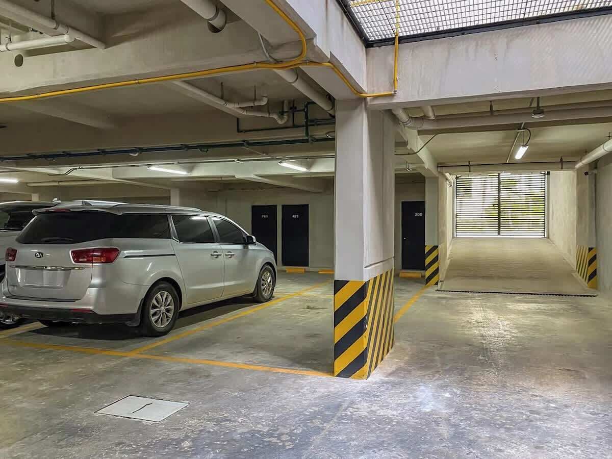 A parking garage with concrete pillars, yellow and black striped safety markings, and a silver car parked in a designated space.