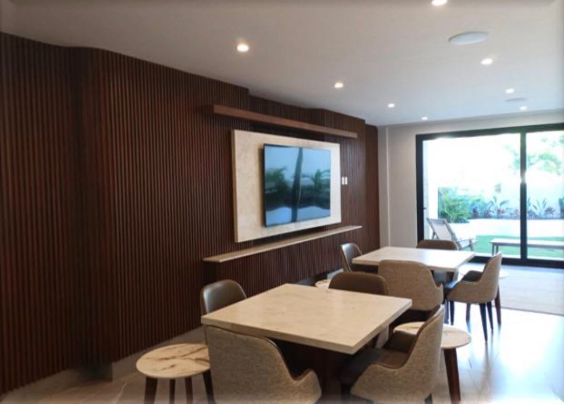 Un espace de repas moderne, doté d’une grande table et de chaises, d’un téléviseur fixé au mur et offrant une vue sur l’extérieur grâce à de grandes fenêtres.