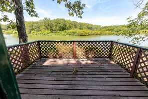 Une terrasse en bois avec une balustrade en treillis, donnant sur un lac paisible et entourée d’une végétation luxuriante.