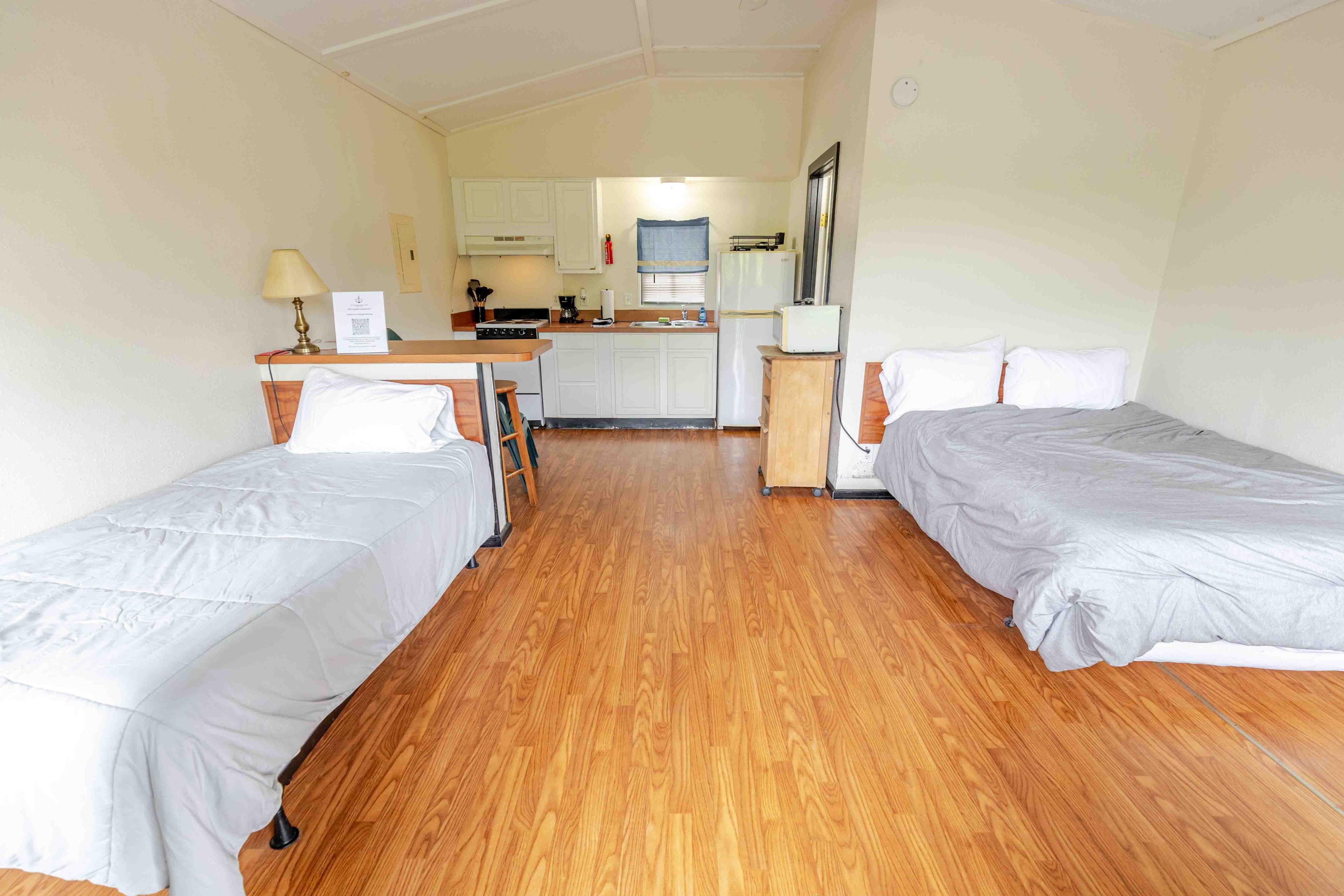 Une chambre d’hôtel compacte avec deux lits simples, une kitchenette et une petite salle de bain.