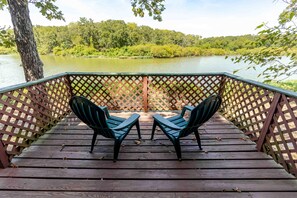 A wooden deck with two chairs facing a lake, surrounded by a lattice fence.