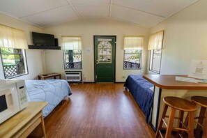 A room with two beds, a desk, a chair, a microwave, and a door with a window.