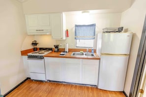 Une cuisine de taille réduite, avec des meubles blancs, une cuisinière, un évier et un réfrigérateur.