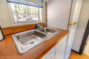 A kitchen with a double stainless steel sink, a window with blinds, and a door to the right.