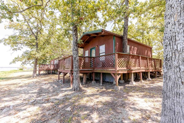A wooden cabin with a deck, surrounded by trees.