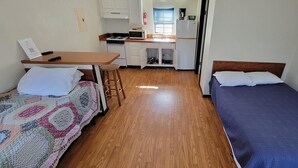 Ein kleines Zimmer mit zwei Einzelbetten, einer kleinen Küchenzeile und Holzboden.