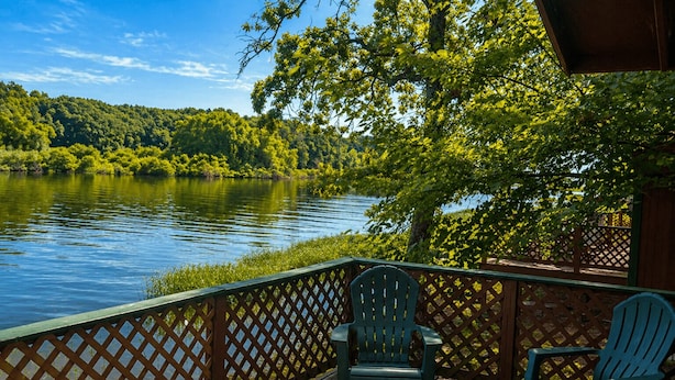 Eine Holzterrasse mit zwei Stühlen mit Blick auf einen See, umgeben von Bäumen und einem Holzzaun.