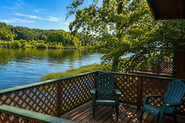 A wooden deck with two chairs overlooking a lake, surrounded by trees and a wooden fence.