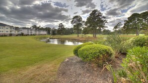 Un parcours de golf avec un étang, des pelouses parfaitement entretenues et un ensemble de bâtiments en arrière-plan.