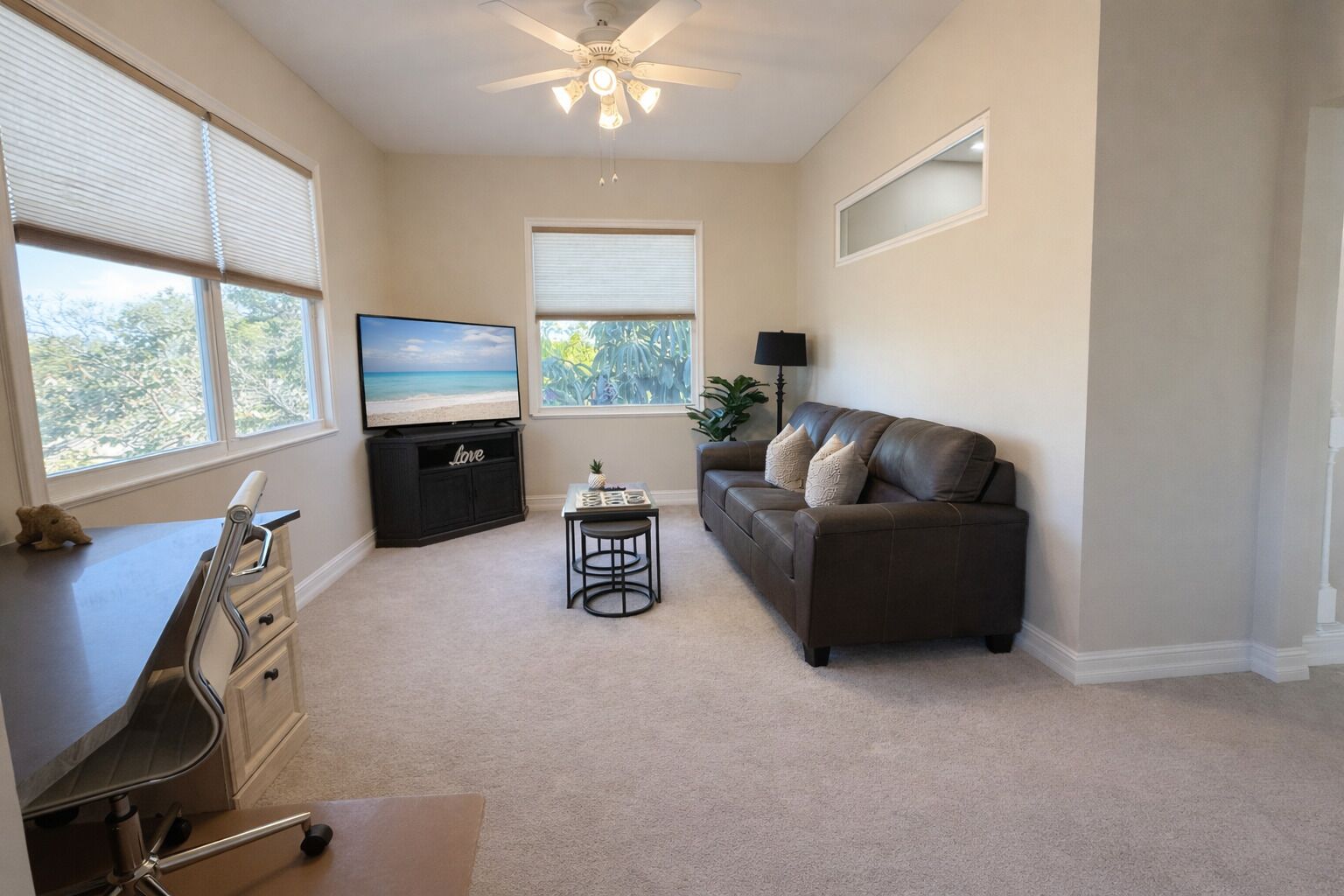 A living room with a TV, a sofa, a desk, and a ceiling fan.