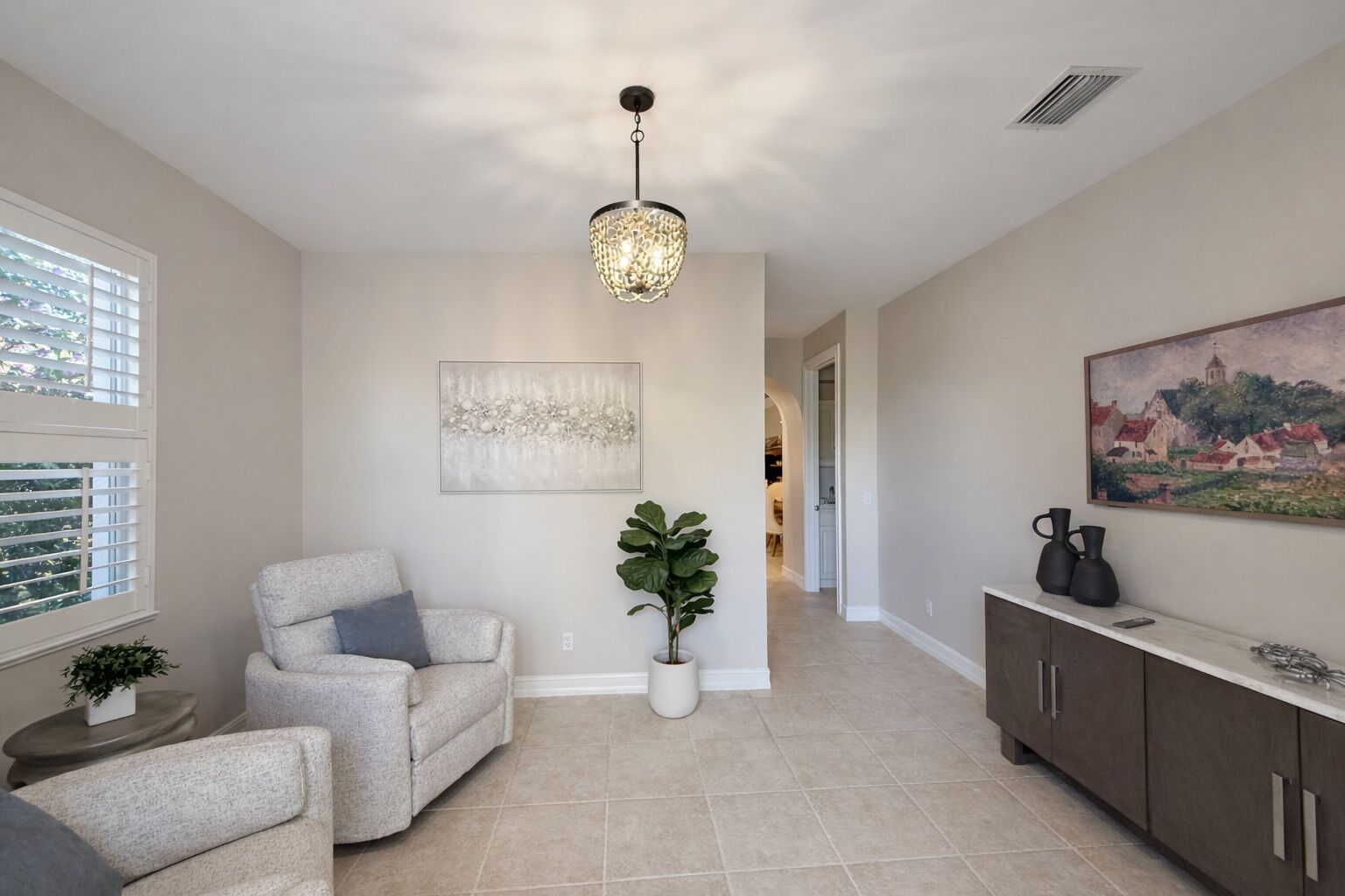 Ein geräumiges Wohnzimmer mit grauem Sofa, einem Blumentopf und einer Chandelier.