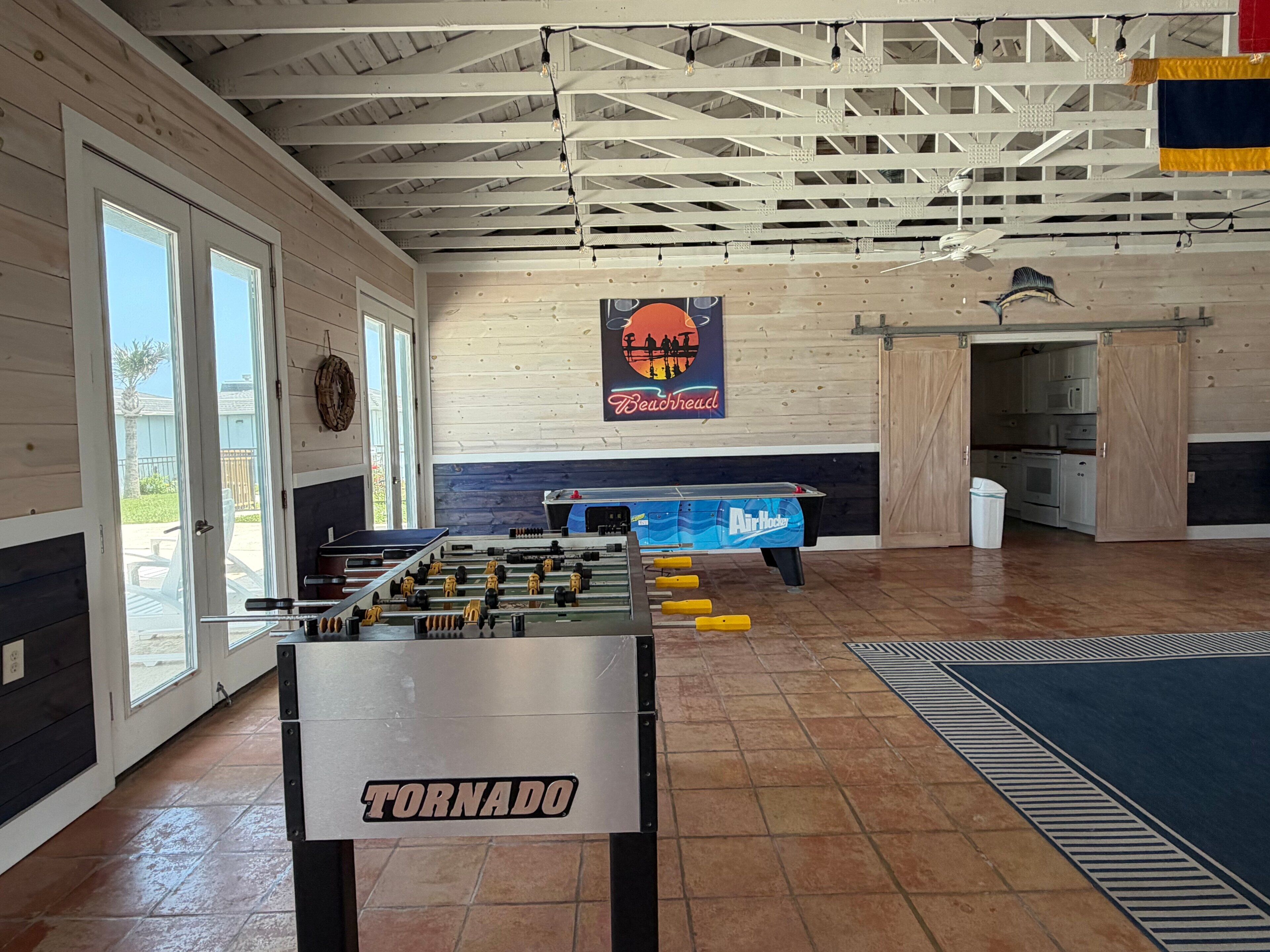 Un espacio interior amplio con mesa de fútbol de mesa, zona de cocina y un cartel que dice 'TORNADO'.