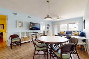 A living room with a round table, chairs, a sofa, a TV, and a ceiling fan. - Shared Heated Pool, Boardwalk to Beach, Golf Cart Access (Port Aransas)