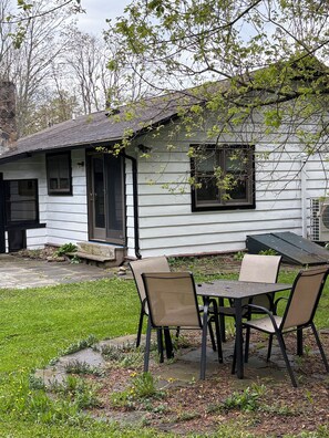 Une maison blanche avec un porche, une table entourée de chaises et un petit jardin.