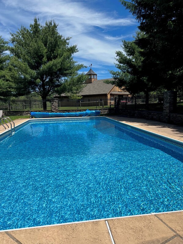 Une piscine rectangulaire à l’eau d’un bleu limpide, entourée d’un mur de pierre et d’une clôture en bois.