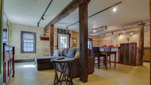A spacious living area with a sofa, a round table, and a wooden beam structure. - Toad Hall Carriage House-quaint family friendly home on a historic estate (Fly Creek)