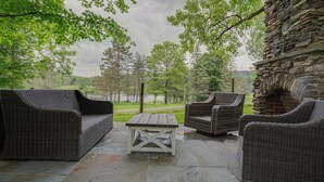 An outdoor patio with wicker furniture, a stone table, and a stone wall. - Toad Hall Carriage House-quaint family friendly home on a historic estate (Fly Creek)