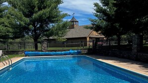 A rectangular swimming pool with clear blue water, surrounded by a stone wall and a wooden fence. - Toad Hall Carriage House-quaint family friendly home on a historic estate (Fly Creek)