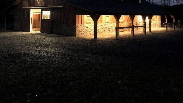 A barn with a large open door and a sloped roof, surrounded by a gravel area. - Toad Hall Carriage House-quaint family friendly home on a historic estate (Fly Creek)