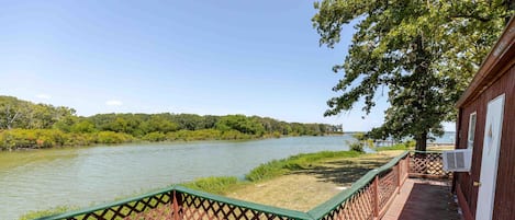 A wooden deck with a lattice railing overlooking a river, with a building on the right.