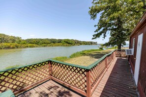 Een houten terras met een lattenhek dat uitkomt op een rivier, met een gebouw aan de rechterkant.