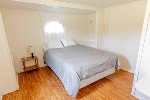 Un dormitorio con una cama individual, una mesita de noche con lámpara y una ventana con cortinas.