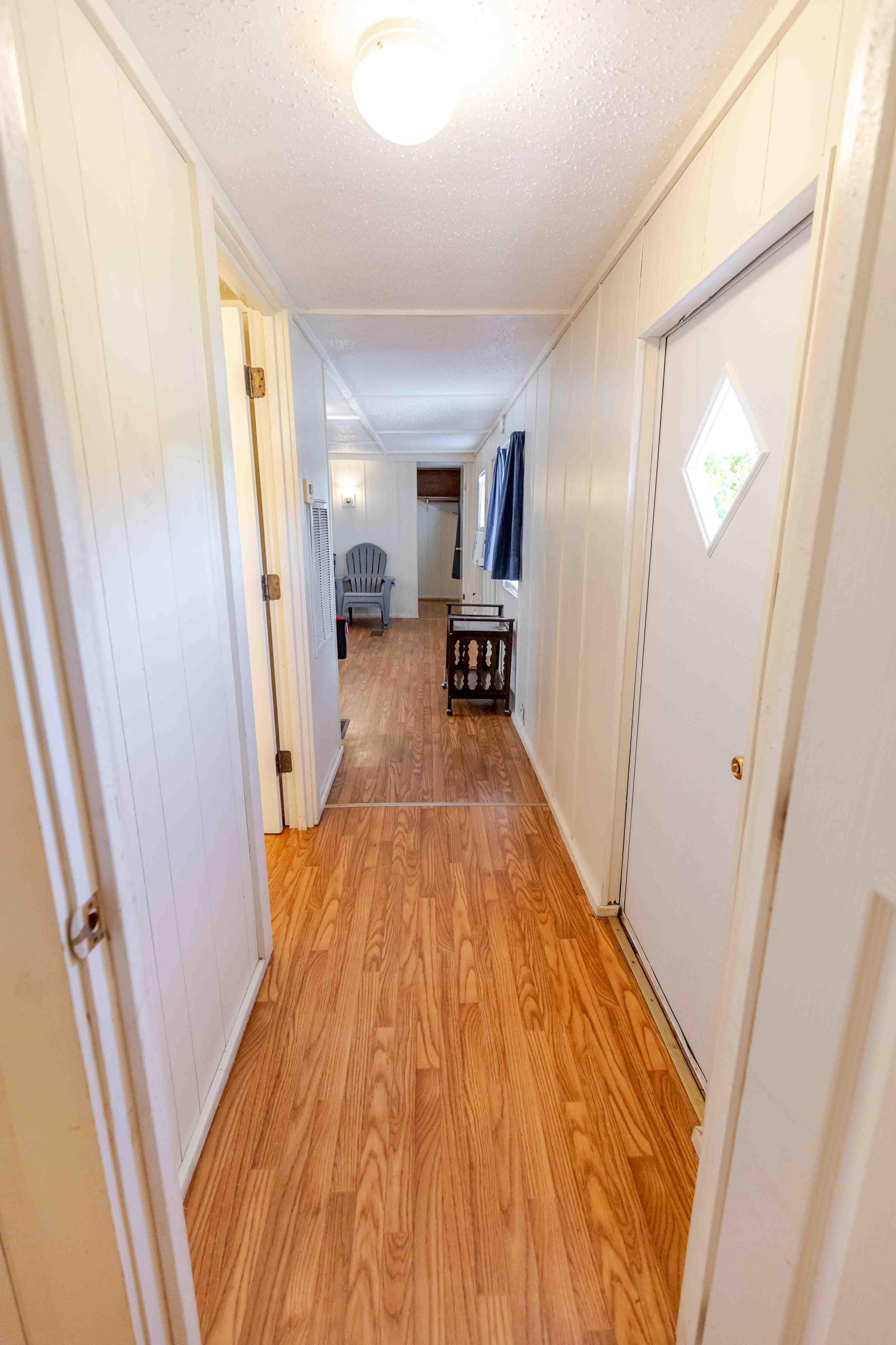 A narrow hallway with wooden flooring, white walls, and a door at the end.