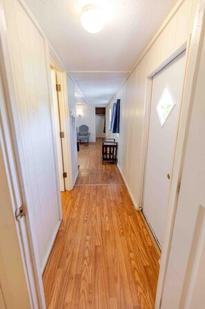 A narrow hallway with wooden flooring, white walls, and a door at the end.