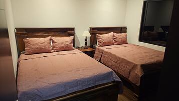 Une chambre avec deux lits, chacun doté d’une tête de lit en bois et d’une couvre-lit rose. Une table de chevet avec une lampe se trouve entre les deux lits.