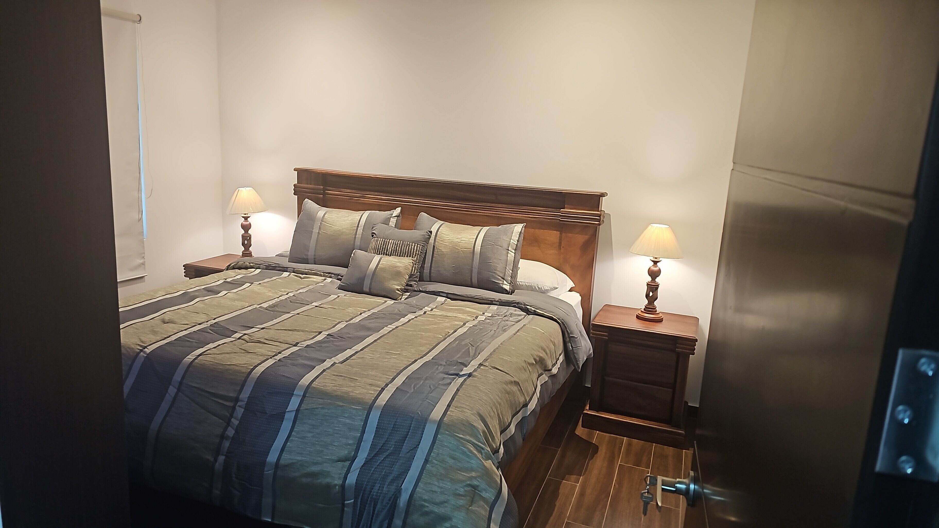 A neatly made bed with striped bedding, two bedside tables with lamps, and a wooden headboard.