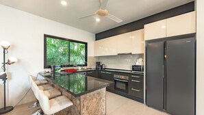 A modern kitchen with a large island, black appliances, and a view of greenery outside. - 4Br Near Pier Private Pool & Garden V246 (Rawai)