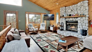 Una sala de estar acogedora con chimenea de piedra, techo de madera y un ventanal grande.