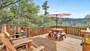 Una terraza de madera con mobiliario exterior, incluyendo una mesa y sillas, y un gran paraguas.