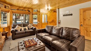 A cozy cabin interior with two leather sofas, a wooden coffee table, and a wooden ceiling.