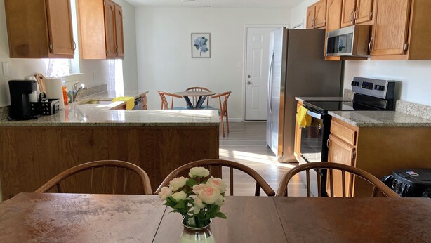 A kitchen with wooden cabinets, a stainless steel refrigerator, a microwave, and a dining area with a table and chairs. - Peaceful & Spacious Family Home (Savannah)