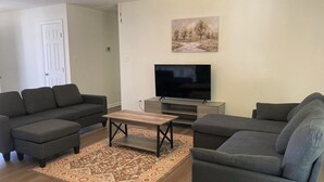 A living room with two sofas, a coffee table, a flat-screen TV on a stand, and a painting on the wall. - Peaceful & Spacious Family Home (Savannah)