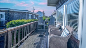 A wooden deck with wicker chairs and a table, overlooking a street with houses and a clear sky. - Cozy Cottage Steps from Beach (Pacific Beach)