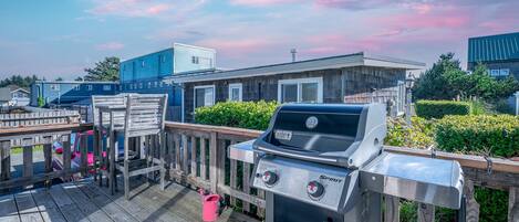 A barbecue grill on a wooden deck with a view of residential buildings and a clear sky.