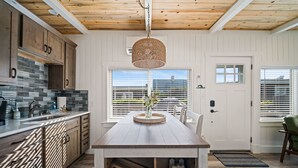 A modern kitchen with wooden cabinets, a stone backsplash, and a large window with blinds. - Cozy Cottage Steps from Beach (Pacific Beach)