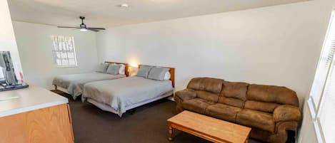 A room with two beds, a brown sofa, a wooden coffee table, and a desk with a computer.