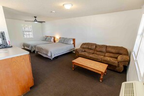 A room with two beds, a brown sofa, a wooden coffee table, and a desk with a computer.