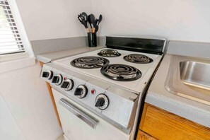 A kitchen with a white stove, four burners, and a stainless steel sink. - Admirals Cabin - Cozy cabin with a waterfront view. (West Tawakoni)