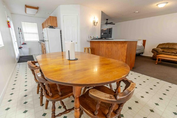 Un coin repas avec une table et des chaises en bois, une cuisine à l’arrière-plan et un salon avec un canapé.