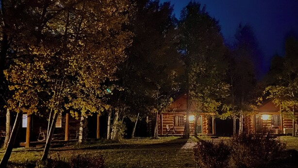 A rustic cabin-style hotel with a wooden exterior, a covered porch, and a well-lit entrance. - Enjoyable 1-bedroom “Mallard” Log Cabin in Ririe (Rigby)