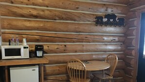 A wooden cabin interior with a wooden table and chairs, a microwave, a coffee maker, and a small refrigerator. - Enjoyable 1-bedroom “Mallard” Log Cabin in Ririe (Rigby)