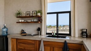 A kitchen with a large window, wooden cabinets, a water dispenser, and a coffee maker. - Trendy studio with incredible ocean views (Todos Santos)